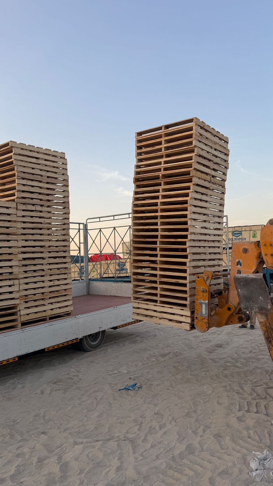 A telehandler loading stacks of wooden pallets onto a flatbed truck