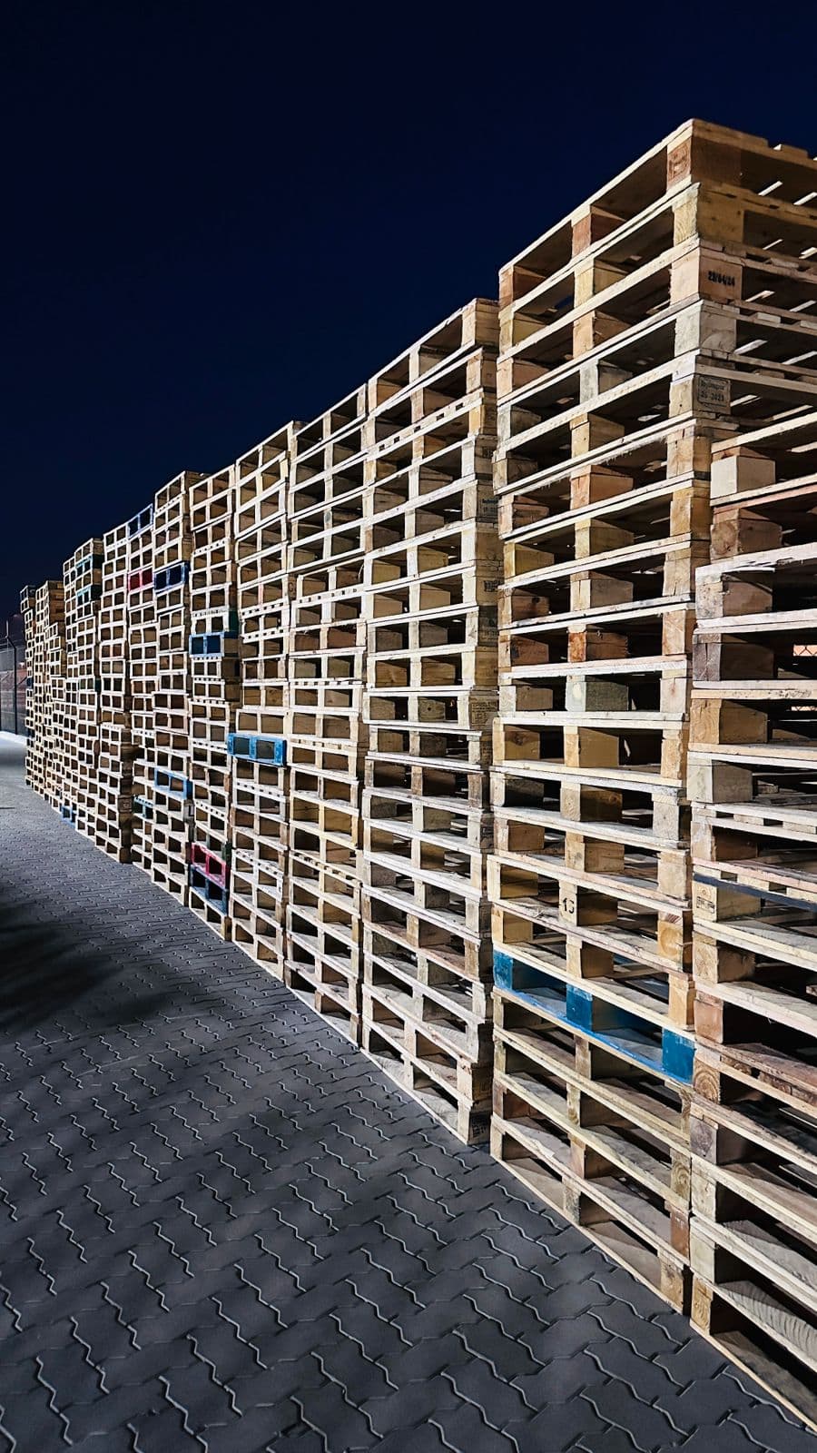 A long wall of used wooden pallets stacked in the yard at night